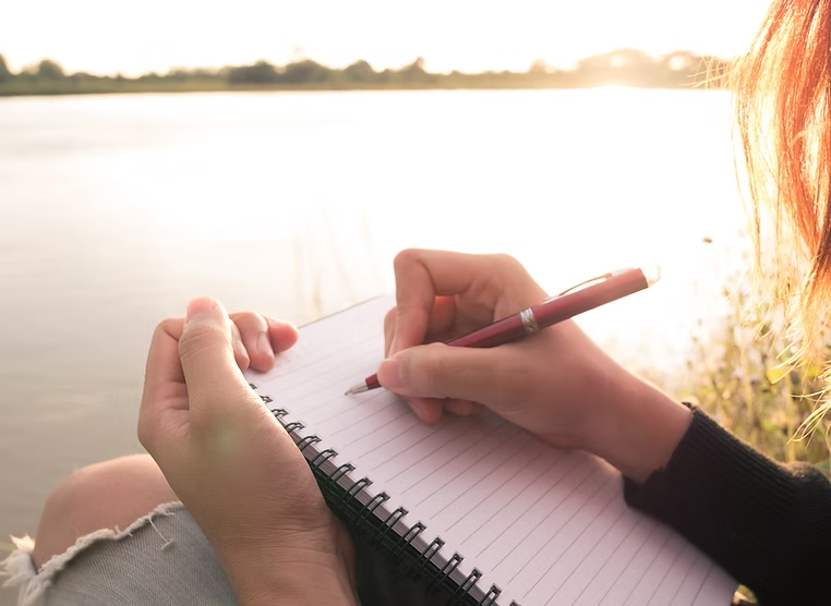 Writing in a notebook beside the water